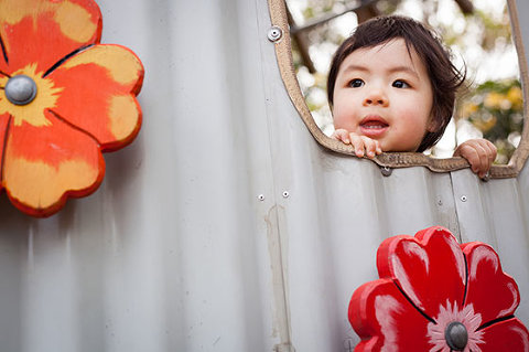 Toddler sticking her head our of whole in playground colour corrected