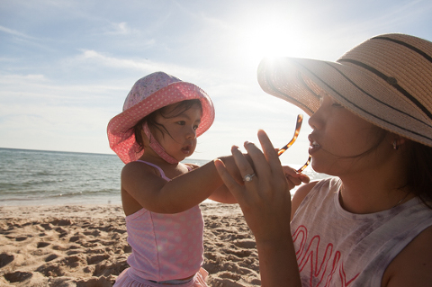 Mum and daughter playing at the beach at sunset with hats on