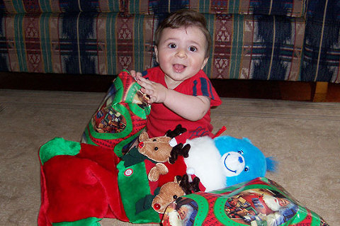 Little baby with lots of christmas presents and happy look on face