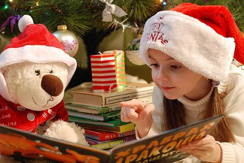 little girl reading christmas story books with presents and a tedd bear