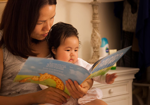 Asian mum reading bedtime story to baby daughter
