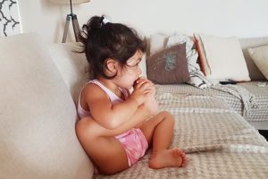Little girl biting her toe while sitting on couch